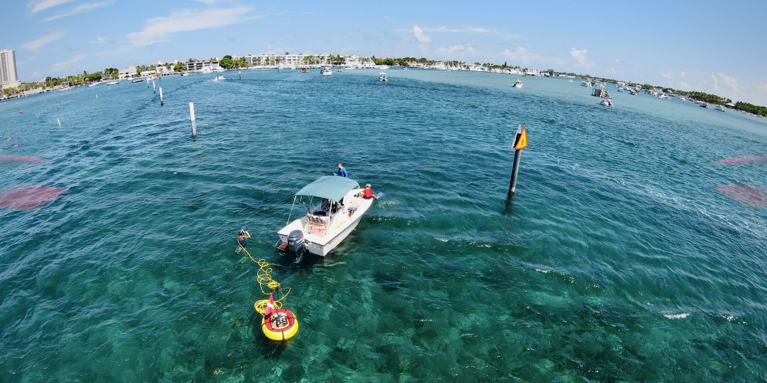 Boat Brownies Third Lung Diving Boat supporting divers using a Brownie’s Third Lung floating dive system with yellow flotation unit and air hoses in clear tropical water near a channel marker.